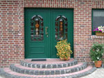 Eine dunkel grne Haustr mit goldenem Griff, verbaut in einem verklinkertem Haus